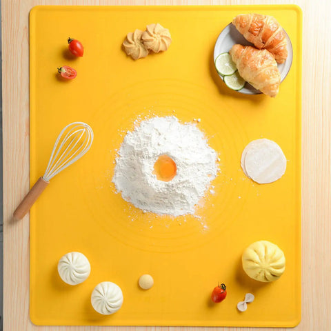 Yellow baking mat with flour, egg yolk, whisk, tomatoes, pastries, and dumplings on wooden table