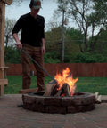 Person using 40 Inch Fire Poker And Log Grabber Set For Fire Pits Must Have Backyard Outdoor Indoor Bonfire Gear Rustproof Two Piece Campfire Tool With Ergonomic Rubber Handles For Safe Easy Firewood Movement on a stone fire pit in a backyard.