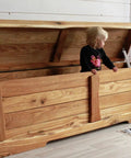 Wooden toy box chest with gas strut hinges; lid open, child standing inside.