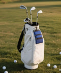 White golf bag on a course holding clubs, featuring blue pockets, standing among scattered balls Portable Golf Ball Storage Bag With Multiple Zip Pockets And 3 Compartments For Easy Organization Of Balls Tees Gloves And Accessories Lightweight Blue Golf Organizer For Men And Women.
