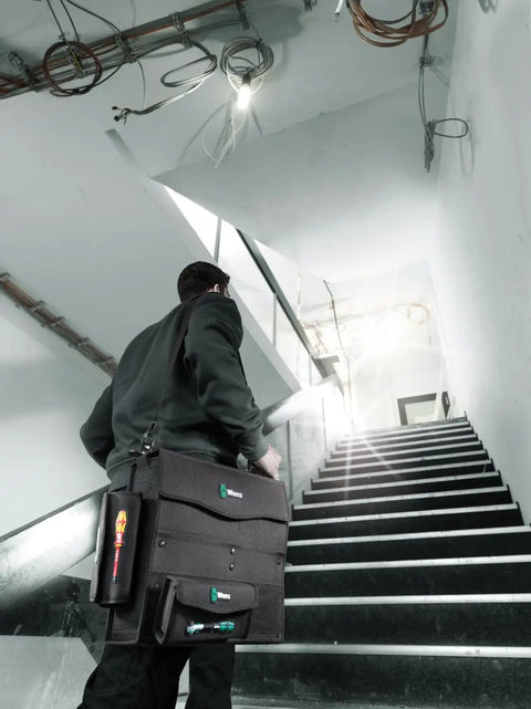Person carrying 2Go 2 Tool Container For On The Go Gear Organization, durable compact storage, ascending stairs, workplace setting.