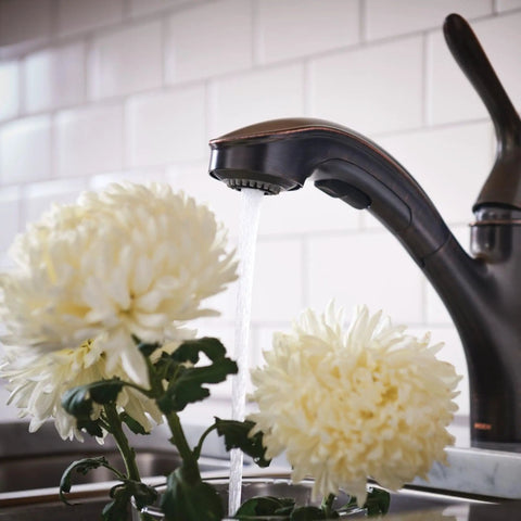 Brecklyn Mediterranean Bronze Single Handle Pull Out Sprayer Kitchen Faucet With Power Clean Tech flowing over white flowers