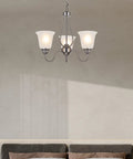 Lit Three Light Chandelier In Brushed Nickel With Frosted Glass Shades above a modern living room sofa