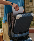 Man placing laptop in Grace Expandable 20 Inch Carry On Hard Shell Luggage with Spinner Wheels, blue, front laptop compartment visible.