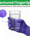 Purple nitrile disposable glove with textured fingertips on hand holding a glass of water.