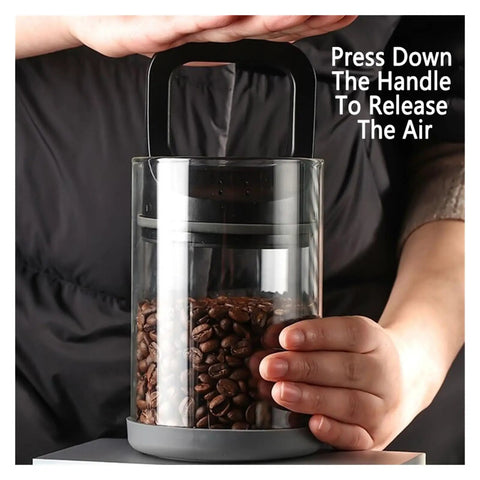 Premium Vacuum Sealed Clear Glass Coffee Bean Canister With Secure Airtight Lid To Keep Kitchen Food Storage And Tea Moisture Proof While Locking Down Freshness For Your Daily Grind In Sleek Black with beans inside and hand pressing the air release handle