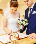 Bride and groom signing a wedding registry at a decorated table, with the bride holding a bouquet and groom in a blue suit.