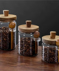 Go Ahead And Upgrade Your Countertop Setup With This Solid Clear Glass Storage Jar Featuring An Airtight Sealed Kitchen Canister And Wooden Spoon For Coffee Beans 900Ml Capacity on wooden table.
