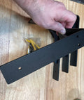 Hand holding Heavy Duty 10x6 Inch Shelf Brackets Set Of 4 Sturdy L Shaped Metal Supports, matte black, with screws in background.