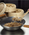 Go-To 14-Inch Carbon Steel Wok With Bamboo Handle for stir frying on stovetop, noodles being stirred