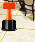 Ultimate Tile Leveling System Kit For Ceramic Floor And Wall Tiles, Reusable Dowels With Wrench, 100 Pcs Flat Pin Fasteners, Keeps Grout Even And Tiles Flat, Speeds Up Installation For DIY Or Pros. Orange tile leveling wedge in black base on ceramic floor