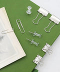 Complete Office Supplies Set With Paper Clips, Binder Clips, And Push Pins in a handy box on a green notebook for office use.