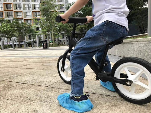 Child on bicycle wearing Disposable Kids Shoe Covers Non Slip Blue 50 Pack 25 Pairs Stretchable Nonwoven Fabric Durable for US Children Size 8 to 13.5 1 to 4 Easy On Breathable Soft Comfort Dustproof Kid Friendly Fit