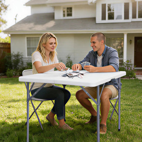 Couple playing cards outdoors on 34-Inch Square Folding Table With Carrying Handle For Indoor Outdoor Picnics Parties Fold-In-Half Design