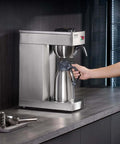 Person using 12 Cup Commercial Drip Coffee Maker With Thermal Vacuum Carafe Keeps Coffee Hot Or Cold All Day No Fuss For Restaurant Office Cafe Stainless Steel Brewer That Brews A Full Pot In About 9 Minutes on countertop.