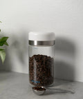 Keep Your Beans Fresh As A Daisy With This Smart Electric Vacuum Seal Coffee Canister And Airtight Storage Jar For Whole Ground Roasts Real Deal Smooth Push Button Operation Durable Borosilicate Glass with coffee beans and measuring spoon.