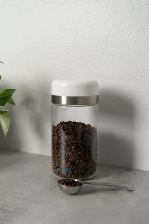 Keep Your Beans Fresh As A Daisy With This Smart Electric Vacuum Seal Coffee Canister And Airtight Storage Jar For Whole Ground Roasts Real Deal Smooth Push Button Operation Durable Borosilicate Glass with coffee beans and measuring spoon.