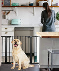 Extra Wide Walk Through Pet Gate With Auto Close Durable Metal Baby And Pet Gate For Stairs And Doorways Forty Point Five Inches Full Width Includes 2 Extension Kits Black installed in a kitchen doorway with a dog sitting in front.