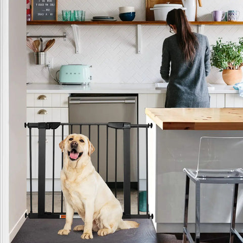 Extra Wide Walk Through Pet Gate With Auto Close Durable Metal Baby And Pet Gate For Stairs And Doorways Forty Point Five Inches Full Width Includes 2 Extension Kits Black installed in a kitchen doorway with a dog sitting in front.