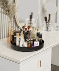 Front view of Ovicar 13-inch black metal Lazy Susan turntable on vanity, filled with makeup bottles, tubes, and brushes.