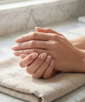 Hands with manicured nails resting on a towel, using Stone Nail File Set With Pumice Stick And Cuticle Pusher For Fingernails And Toenails Care.
