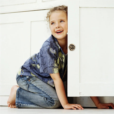Child playing and smiling near a white cabinet with Vintage Rose Flower Cabinet Knobs Two Pack Classic Floral Drawer Pulls.
