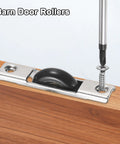 Installation of barn door roller on wooden surface with screwdriver, showing metal bracket and black wheel sliding mechanism.