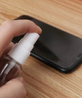 2 Pack 1Oz Clear Plastic Travel Spray Bottles Refillable Mini Spritzers For Travel Cleaning Gardening Skin Care Essential Oils And Perfume With Protective Caps Leak Free On The Go being used to clean a smartphone.