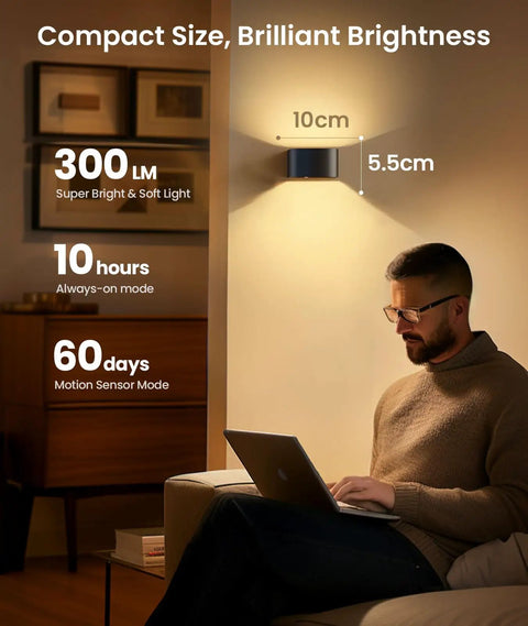 Man using laptop under Motion Sensor Wall Light With Remote Control No Fuss Three Color Modes Wireless LED Indoor Up And Down Wall Sconce 5000mAh Rechargeable Battery Powered Brightness Adjustable Two Pack illuminated in a room.