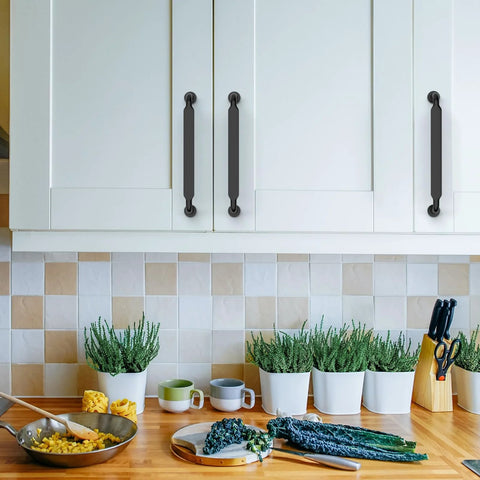 10 Pack 5 Inch Matte Black Kitchen Cabinet Handles And Drawer Pulls installed on white cupboards in a kitchen setting with plants and utensils.