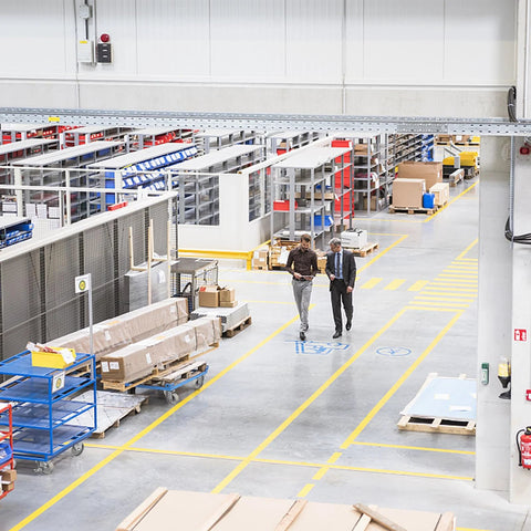 Interior of a warehouse with workers walking, surrounded by shelving units and heavy duty steel casters on carts for industrial use.