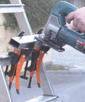 4-Piece Hands-Free Pliers And Grip Holder Set holding a metal rod against a ladder while a saw cuts through, showing secure work setup.
