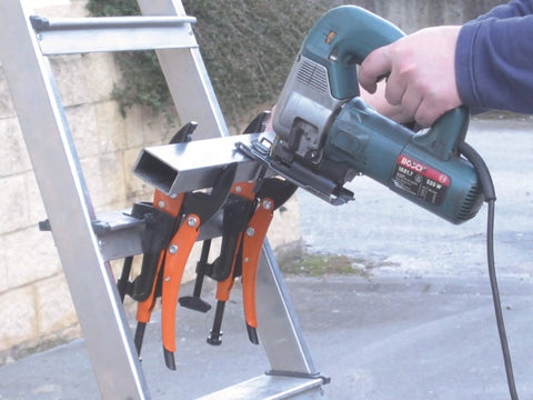 4-Piece Hands-Free Pliers And Grip Holder Set holding a metal rod against a ladder while a saw cuts through, showing secure work setup.