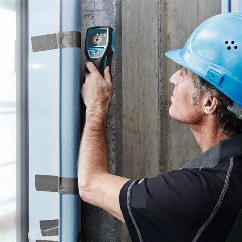 A man uses The Real Deal Digital Wall Scanner And Floor Detection Tool on a concrete wall to locate hidden wires and pipes.