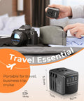 Universal Travel Power Adapter With 2 USB C Ports And 2 USB A Ports Worldwide Wall Charger shown next to camera and travel bag.