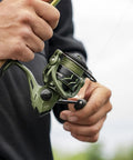 Spartacus II Spinning Reel Sealed Carbon Fiber Build 22 Lb Max Drag 7 Plus 1 Stainless Bearings Five Point Two To One Gear Ratio Saltwater And Freshwater Ready Size 500 And 1000 For Ice Fishing. Angler holding reel for freshwater and saltwater use.