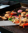 Grilled vegetables and chicken being turned with a stainless steel spatula on a barbecue grill