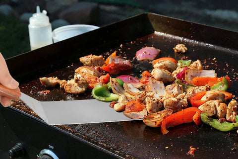 Grilled vegetables and chicken being turned with a stainless steel spatula on a barbecue grill