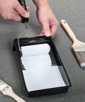 Person using roller on 4 Inch Paint Tray Pan Set 12 Pack Black Spill Resistant Mini Trays With Dual Wells For Rollers And Roller Pan Disposable