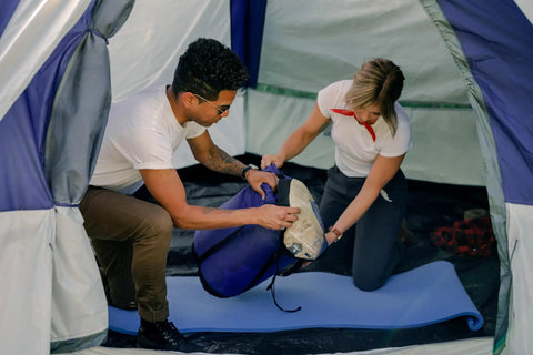 Two campers place gear inside a tent with a Pack Lite Camping and Backpacking Sleeping Pad Lightweight Closed Cell Foam Mat.