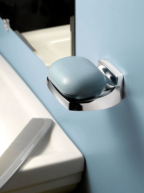 Chrome wall-mounted soap dish with blue soap bar, shown against light blue bathroom wall, near a sink.