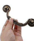 Hand holding a vintage drawer pull from Six Pack Drop Cabinet Drawer Pulls With 3-3/4 Inch Center To Center Bail Handles In Yellow Bronze Finish