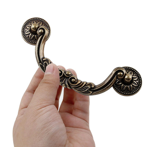 Hand holding a vintage drawer pull from Six Pack Drop Cabinet Drawer Pulls With 3-3/4 Inch Center To Center Bail Handles In Yellow Bronze Finish