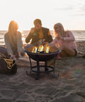 Beach scene with Extra Large Fire Pit BBQ Grill Bowl with mesh screen, tote bag, and friends enjoying a bonfire.