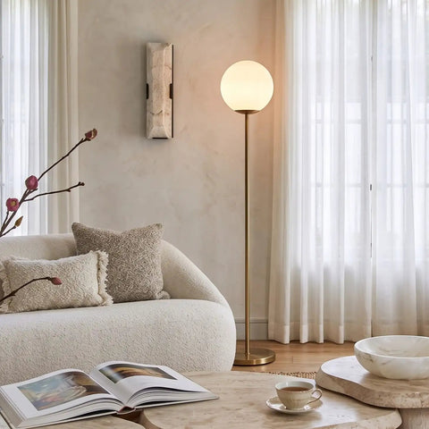 Luna LED Floor Lamp Dope Modern Tall Light For Living Rooms And Home Offices With Frosted Glass Globe Mid Century Style Standing Lamp In Brass Gold Finish Perfect For Reading In The Bedroom And Cozy Vibes next to a sofa in a cozy living room.