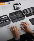Hands typing near One Hundred Piece Precision Screwdriver Set With Ratchet And Magnetic Tweezers For Electronics PCs Laptops And Tablets DIY Friendly Desktop Mini Tool Station With Bits For Repair And Household Fixes.