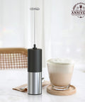 Handheld Electric Milk Frother And Drink Mixer Creates Rich Creamy Foam In Seconds With Stainless Steel Whisk next to a creamy coffee drink.