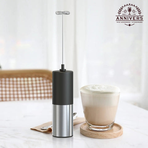 Handheld Electric Milk Frother And Drink Mixer Creates Rich Creamy Foam In Seconds With Stainless Steel Whisk next to a creamy coffee drink.