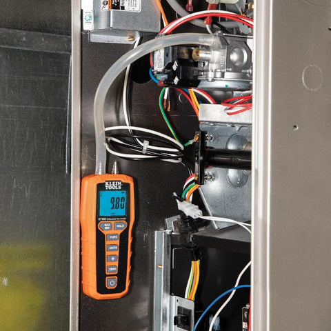 Klein Tools ET180 digital manometer with orange housing and backlit LCD, connected to tubing inside metal cabinet.