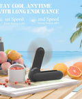 Black 2 In 1 Portable Handheld Fan USB Rechargeable Personal Mini Fan With 8 To 15 Hours Run Time Battery Operated on a table by the beach